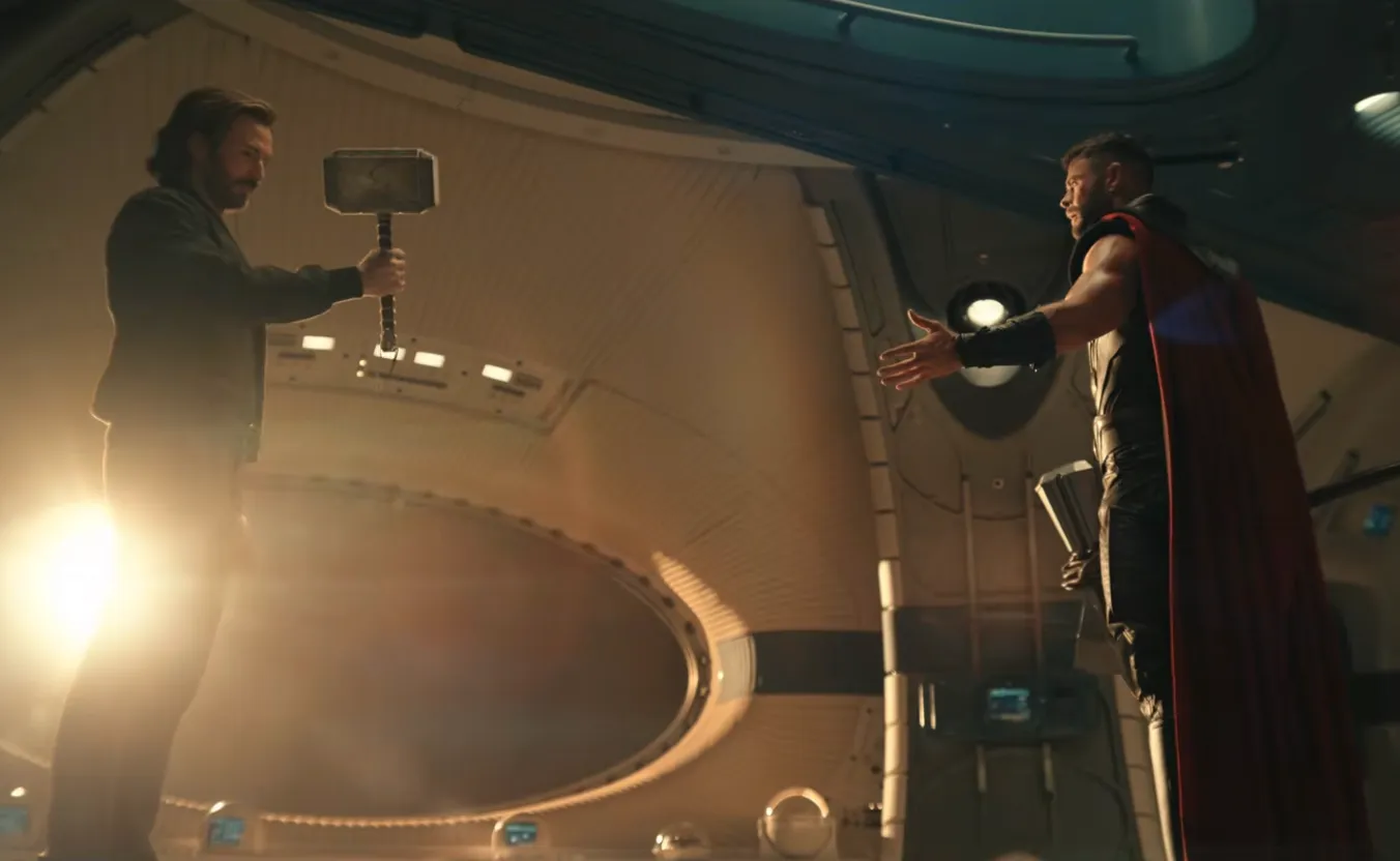Two men in a spacecraft interior, one holding a tool and the other reaching out.