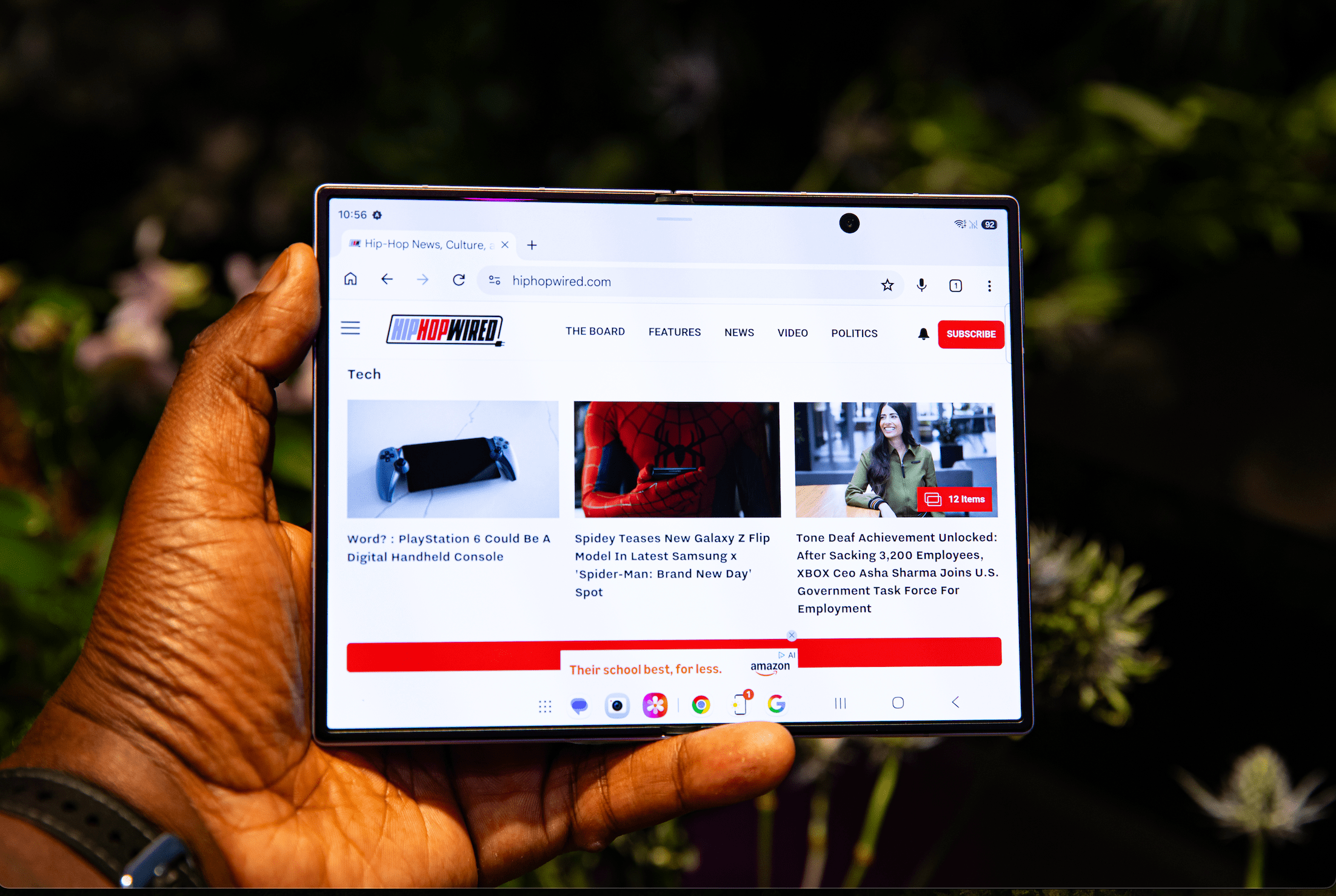 A person holding a tablet displaying the Hiphoprised.com website, which features news and articles about technology, entertainment, and politics.