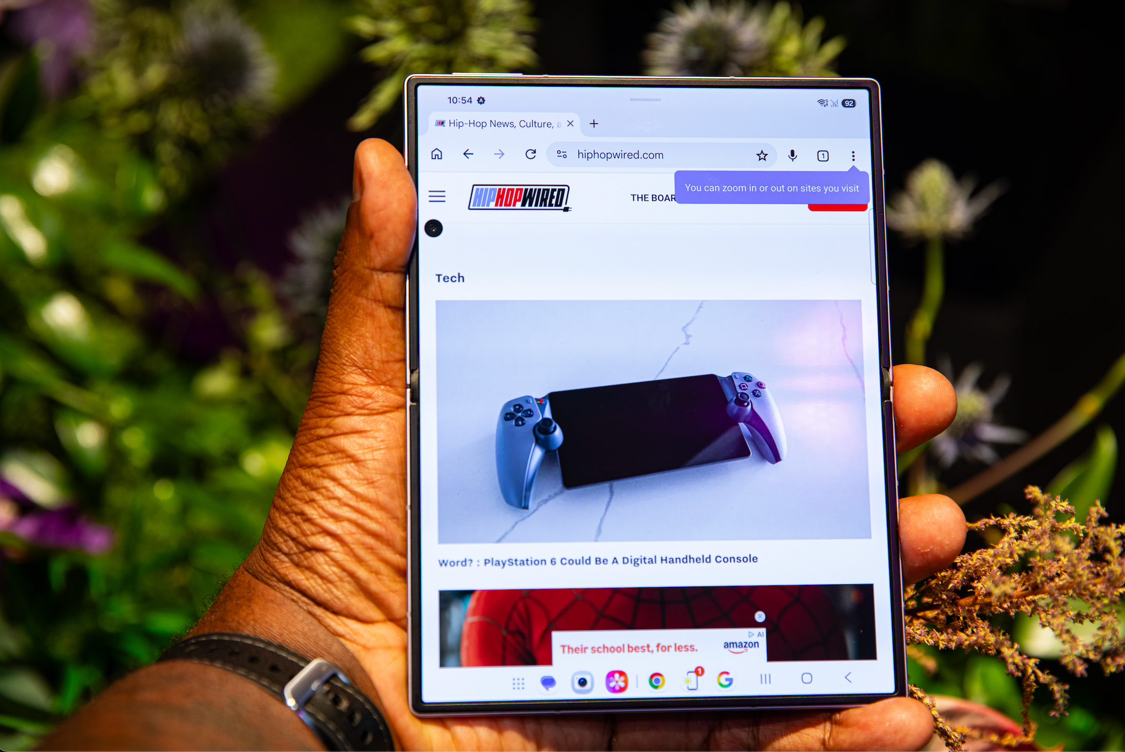 A hand holding a tablet displaying a PlayStation 6 controller on a website called HipHopWired.com