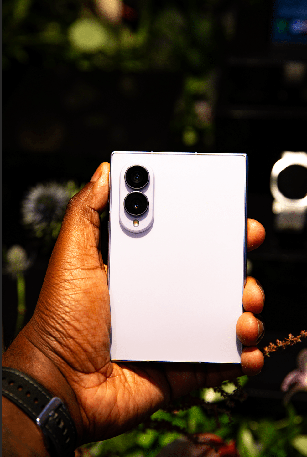 A hand holding a white smartphone with dual cameras and a black frame against a blurred green background.