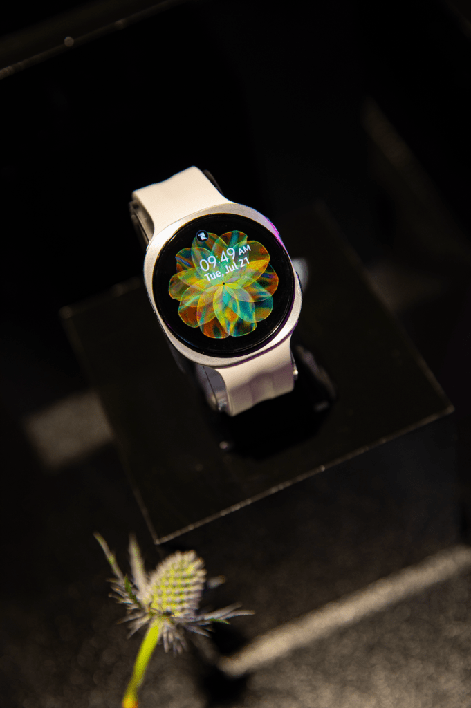 A smartwatch display showing the time and date, with a colorful abstract flower-like design on the screen.