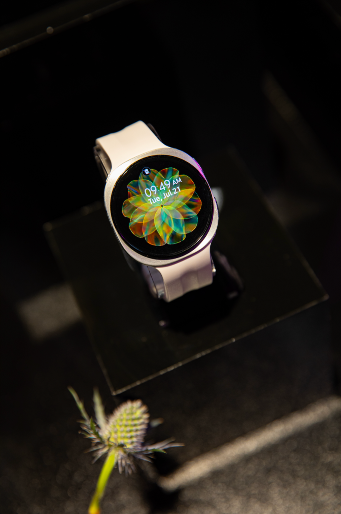A smartwatch display showing the time and date, with a colorful abstract flower-like design on the screen.