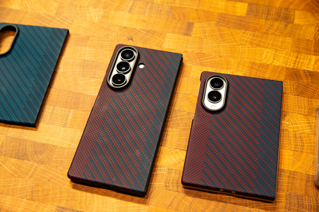 Two black smartphone cases with a carbon fiber pattern and dual camera lenses on a wooden surface.