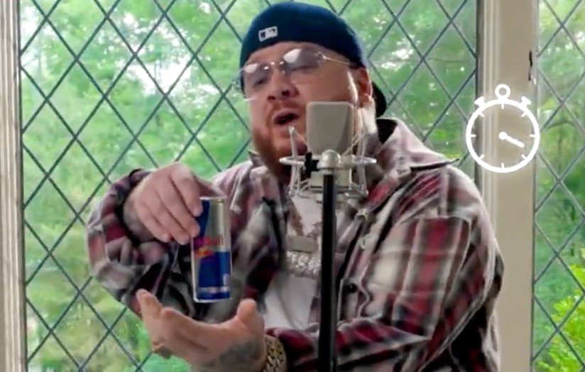 A person wearing a black hat and plaid shirt speaking into a microphone while holding a beverage can.