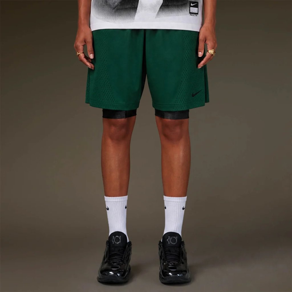 Green Nike basketball shorts with black and white accents, worn with white Nike socks and black Nike sneakers.