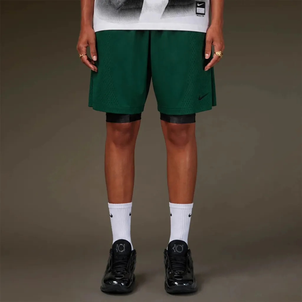 Green Nike basketball shorts with black and white accents, worn with white Nike socks and black Nike sneakers.
