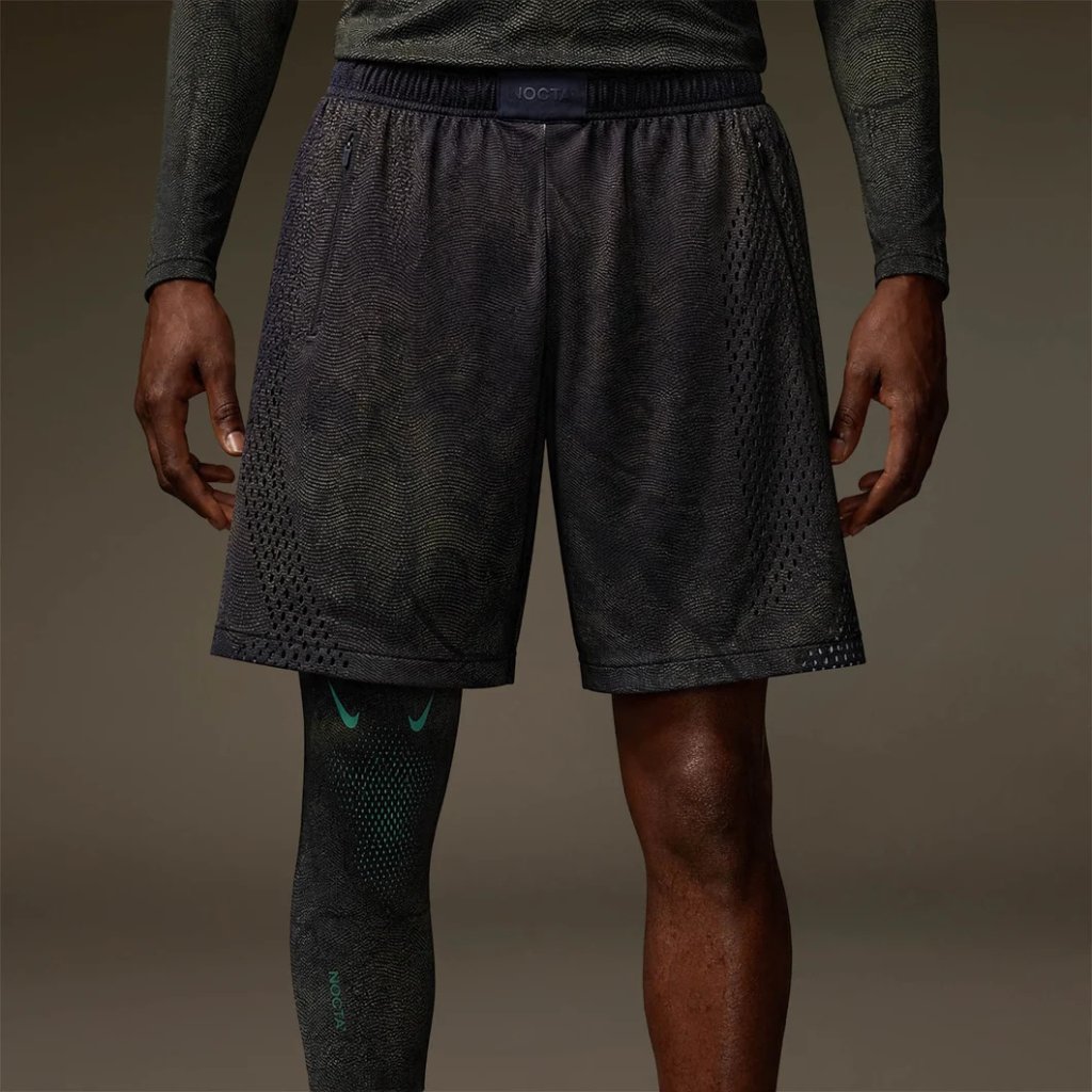A person wearing black athletic shorts and compression socks, standing in a dark setting.