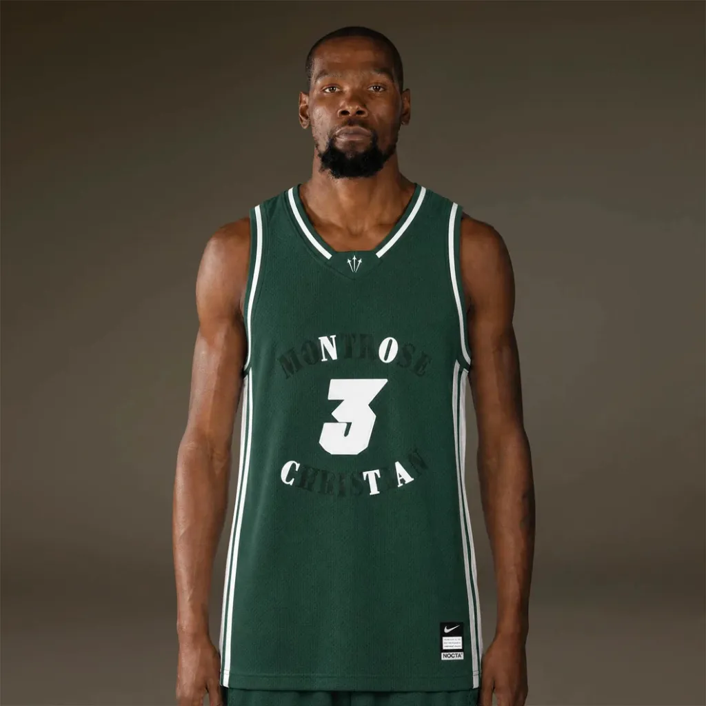 A man wearing a green basketball jersey with the text "MENTOR 3 CHRISTA" standing against a dark background.