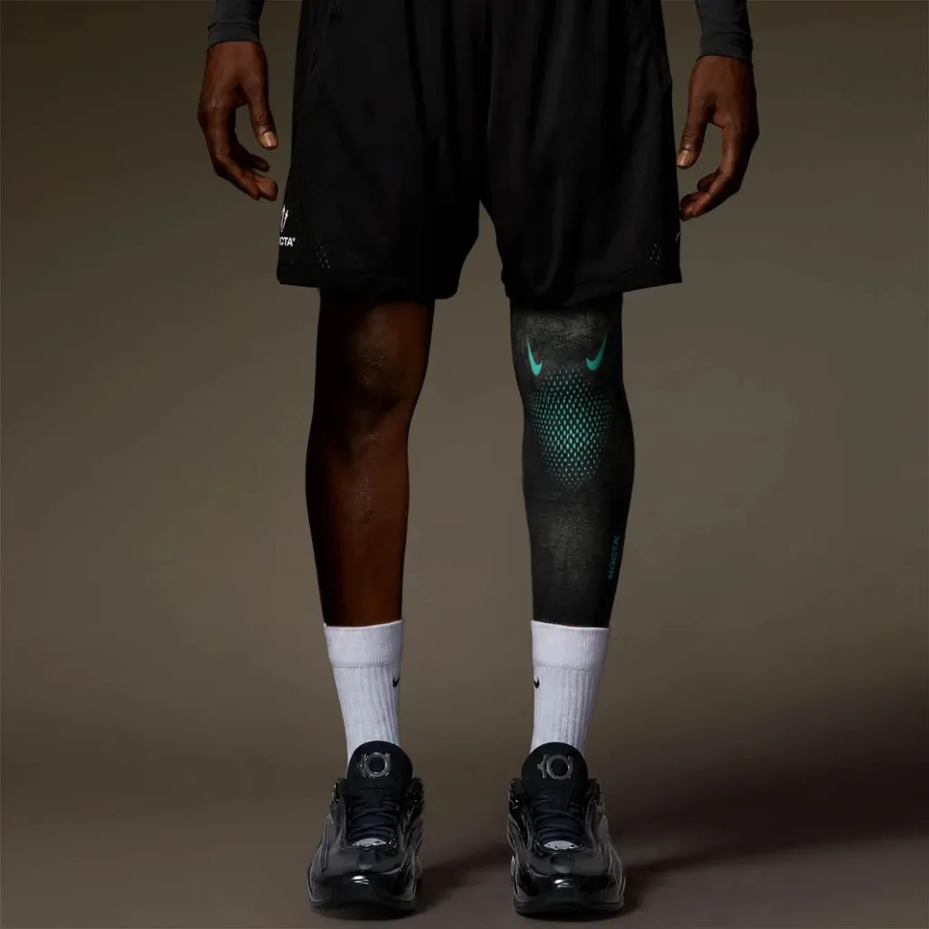 A person wearing black athletic clothing and Nike sneakers, with a patterned compression sleeve on their leg.