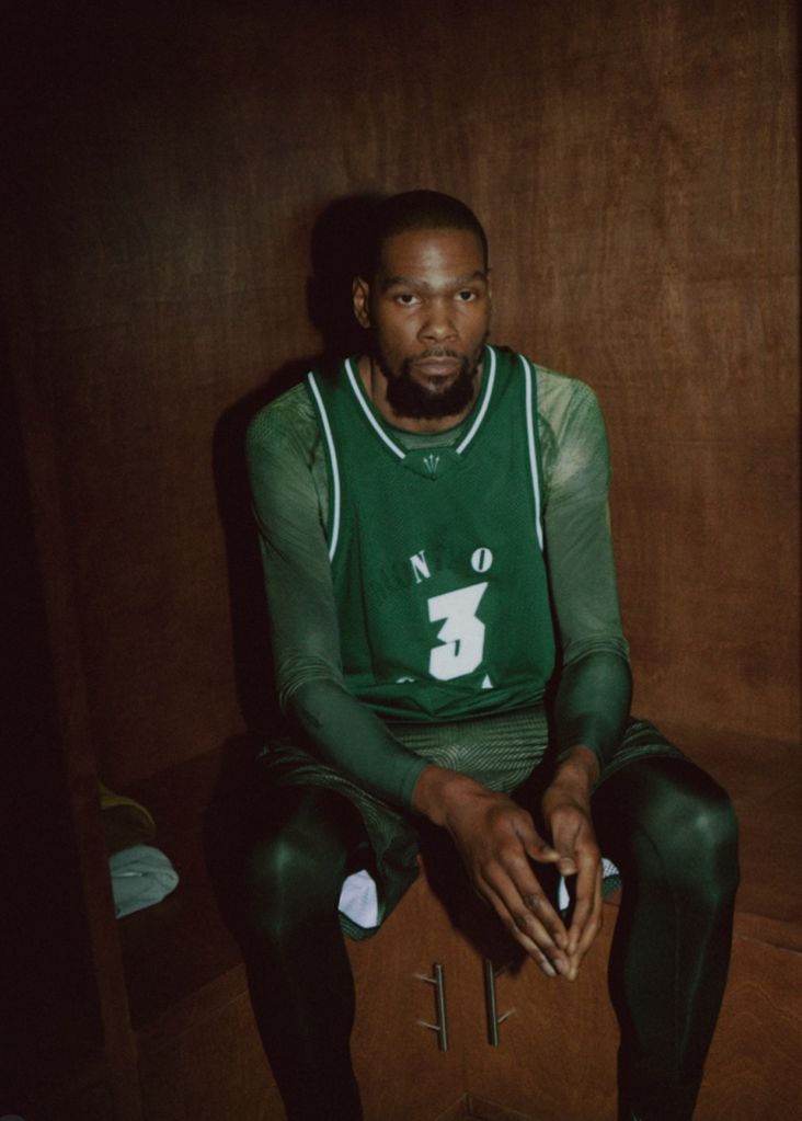 A man wearing a green jersey with the number 3 sits in a dimly lit room, looking directly at the camera.