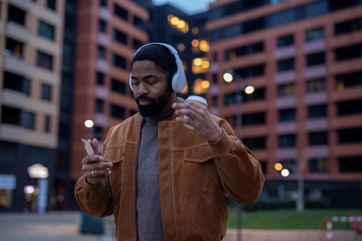 Young man enjoying music walking in city with coffee