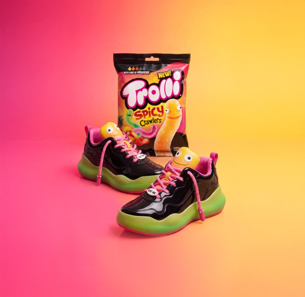 Pair of colorful sneakers with Trolli Spicy Crawlers snack bag on a vibrant pink and yellow background.