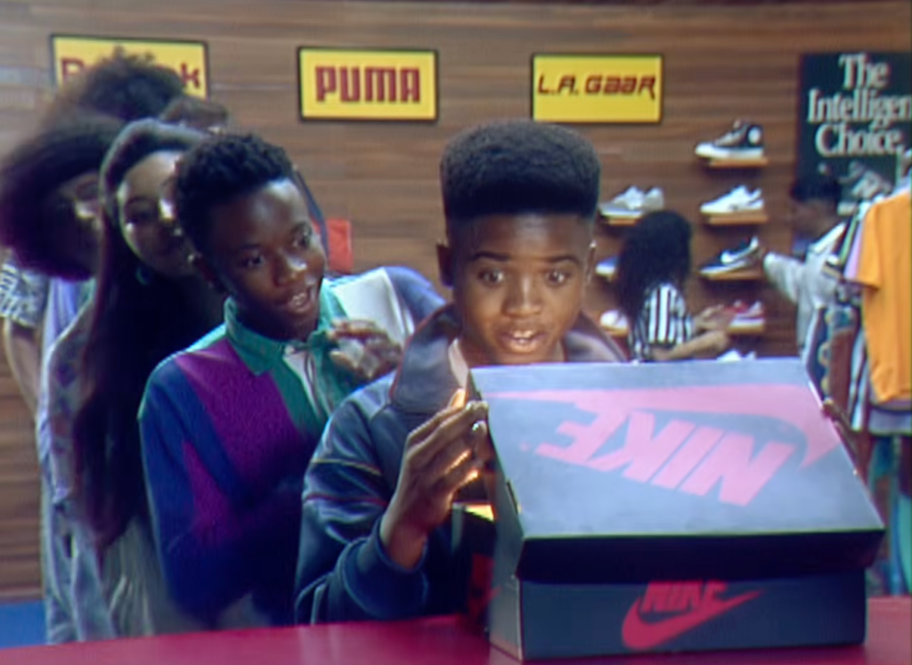 Two young Black boys standing in a shoe store, one holding a Nike box and looking excited.