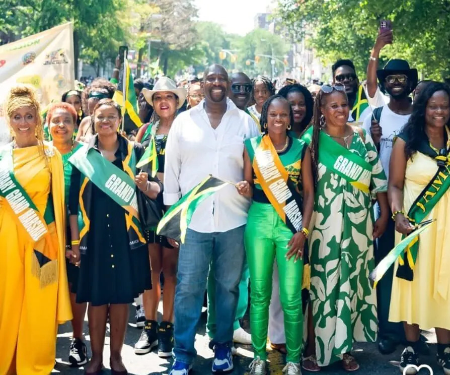 A large group of people wearing Jamaican-themed clothing and holding Jamaican flags, celebrating at what appears to be a parade or festival.