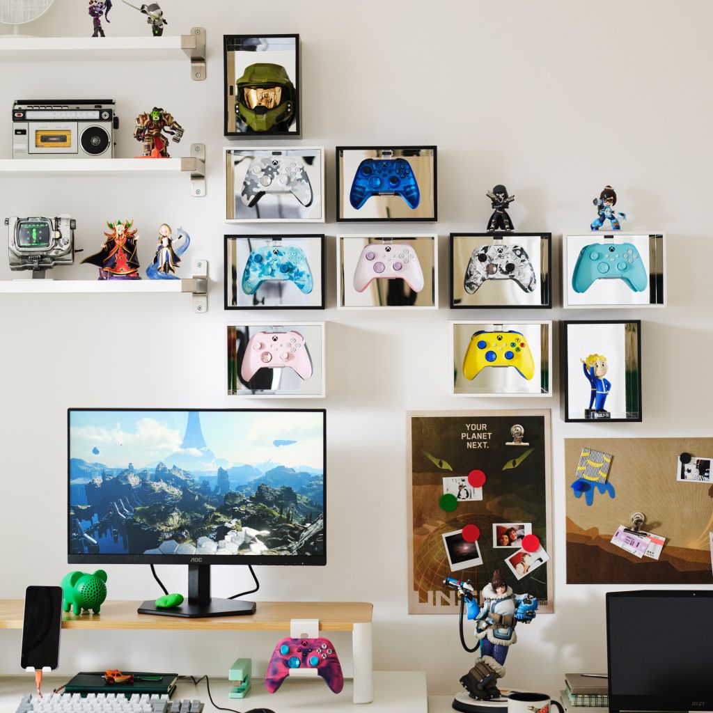 A wall display featuring various gaming-related items, including framed controllers, figurines, and a large landscape image of a futuristic city. The display also includes a bulletin board with photos and other memorabilia.