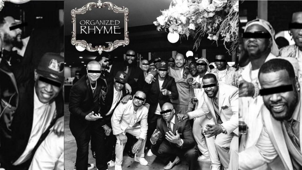 A group of people, mostly men, posing together in a black and white photograph. The sign above them reads "ORGANIZED RHYME".