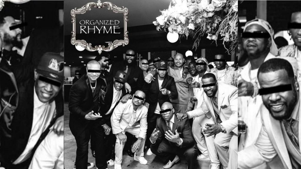 A group of people, mostly men, posing together in a black and white photograph. The sign above them reads "ORGANIZED RHYME".